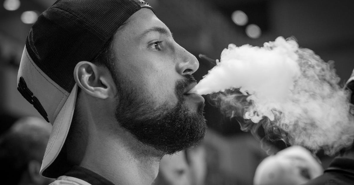 Artistic black and white close-up of a man exhaling vapor, emphasizing modern lifestyle.